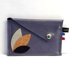 May include: A small, dark blue leather envelope clutch with a decorative leaf design in shades of brown, white, and black. The clutch has a silver snap closure and a small label that says "100%".