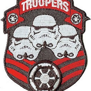 以下が含まれることがあります： 白のストームトルーパーのヘルメットが3つと、白いバナーに「TROOPERS」という文字が書かれた、茶色と赤の刺繍パッチ。パッチには、黒と白の帝国のシンボルも描かれている。