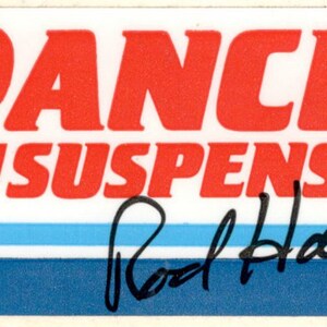 May include: A white sticker with red text that reads "RANCHO SUSPENSION" and a black signature that reads "Rod Hall". The sticker has two blue stripes.