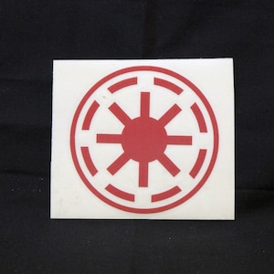 Könnte beinhalten: Ein roter und weißer Aufkleber mit dem Symbol des Galaktischen Imperiums. Das Symbol ist ein Kreis mit einem Sonnenstrahlenmuster im Inneren.