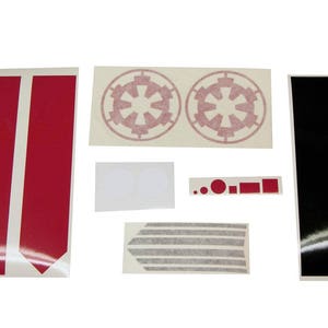 May include: A set of red, black, and gray decals for customizing a model. The decals include two Imperial symbols, two red stripes, a black stripe, and a gray stripe.