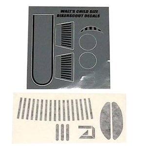 Può includere: Un foglio di adesivi in ​​bianco e nero per una motocicletta per bambini. Gli adesivi includono un motivo a strisce, un motivo a griglia e un motivo circolare. Il testo "Walt's Child Size Bikerscout Decals" è stampato sul foglio.
