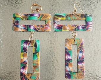 May include: A pair of rectangular dangle earrings with a colorful marbled design. The earrings feature a gold-colored hook and a smaller rectangular pendant hanging below. The marbled pattern includes green, purple, yellow, and brown hues.