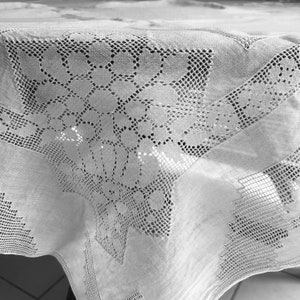 May include: A white tablecloth with a delicate lace pattern. The lace is a geometric design with small circles and squares.