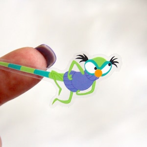Peut inclure: Un autocollant transparent avec un insecte vert de dessin animé portant des vêtements violets et de grands yeux. L'insecte a une longue queue rayée.