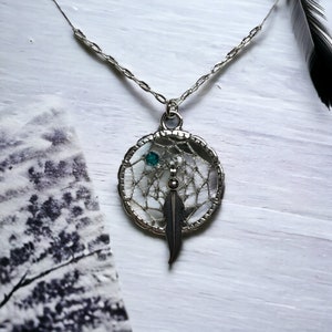 May include: Silver necklace with a dreamcatcher pendant featuring a turquoise gemstone and a feather.
