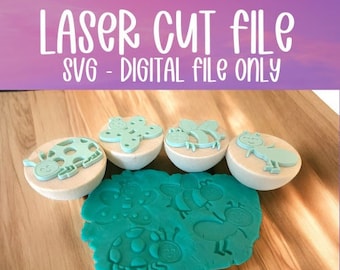 May include: A set of five laser cut wooden stamps featuring a ladybug, a butterfly, a bee, an ant, and a flower. The stamps are arranged on a wooden surface with a green play dough mat showing the impressions of the stamps.