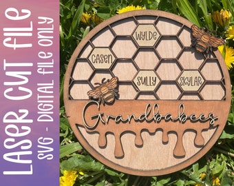 May include: A wooden round sign with a honeycomb design, featuring the word "Grandbabees" and the names "Cason", "Wylde", "Sully", and "Skylar". Two wooden bees are attached. The sign also includes the text "LASER CUT FILE SVG - DIGITAL FILE ONLY".