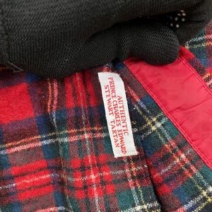 Puede incluir: Una tela de cuadros rojos, negros y verdes con una etiqueta blanca que dice "Authentic Prince Charles Edward Stewart Tartan".