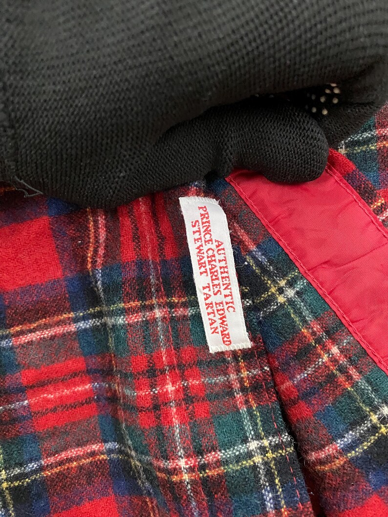 Puede incluir: Una tela de cuadros rojos, negros y verdes con una etiqueta blanca que dice "Authentic Prince Charles Edward Stewart Tartan".