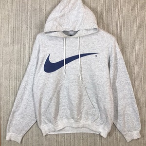 Peut inclure: Un sweat &agrave; capuche gris avec un grand logo Nike swoosh bleu sur le devant. Le sweat-shirt a une poche kangourou et une capuche &agrave; cordon.
