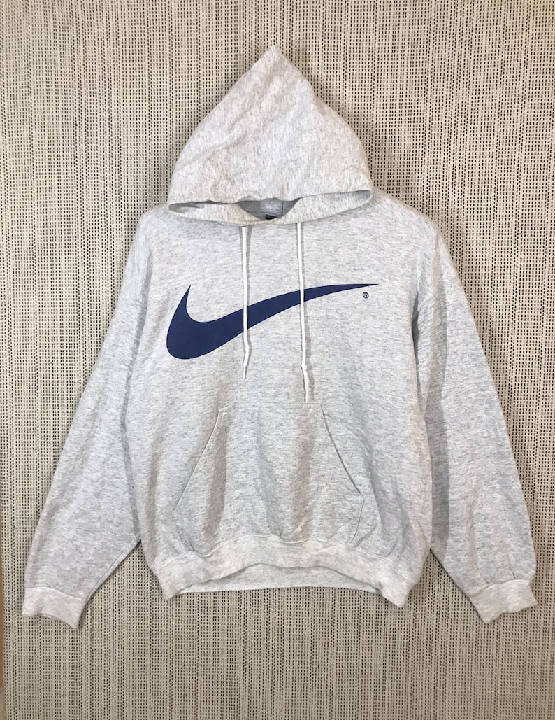 Peut inclure: Un sweat &agrave; capuche gris avec un grand logo Nike swoosh bleu sur le devant. Le sweat-shirt a une poche kangourou et une capuche &agrave; cordon.
