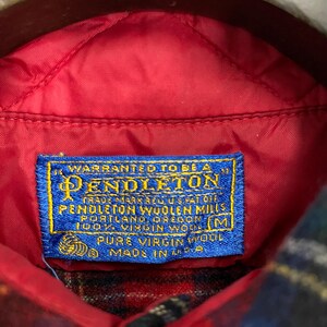Puede incluir: Una etiqueta azul y blanca con el texto "WARRANTED TO BE A PENDLETON TRADE MARK REG US PAT OFF PENDLETON WOOLEN MILLS PORTLAND, OREGON 100% VIRGIN WOOL PURE VIRGIN WOOL MADE IN U.S.A." y una talla "M" en la esquina inferior derecha.