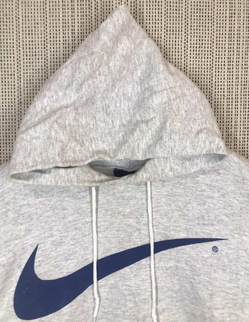 Peut inclure: Sweat-shirt &agrave; capuche gris avec un grand logo Nike swoosh bleu marine sur le devant. Le swoosh est soulign&eacute; de blanc.