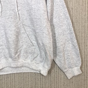 Peut inclure: Sweat-shirt &agrave; capuche gris avec une bande bleue sur la poitrine et un petit logo sur le c&ocirc;t&eacute; gauche. Le sweat-shirt a une poche kangourou et des manches longues.