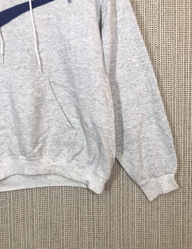 Peut inclure: Sweat-shirt &agrave; capuche gris avec une bande bleue sur la poitrine et un petit logo sur le c&ocirc;t&eacute; gauche. Le sweat-shirt a une poche kangourou et des manches longues.