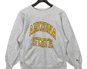 May include: A gray Champion sweatshirt with the text "ARIZONA STATE" in yellow on the front. The sweatshirt has a crew neck and long sleeves.