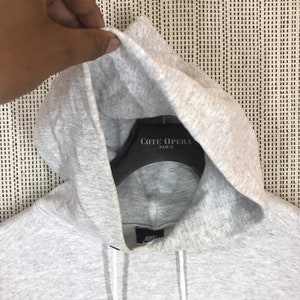 Peut inclure: Sweat-shirt &agrave; capuche gris avec un logo Nike swoosh bleu marine et le mot "Nike" en lettres blanches sur le devant. La capuche est doubl&eacute;e de tissu gris et a un cordon de serrage blanc. Le sweat-shirt a une &eacute;tiquette blanche avec le texte "C&ocirc;te Opera Paris" dessus.