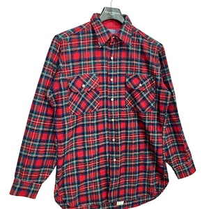 Puede incluir: Camisa de franela a cuadros rojos y verdes con mangas largas y cierre de botones. La camisa tiene dos bolsillos de solapa en el pecho.