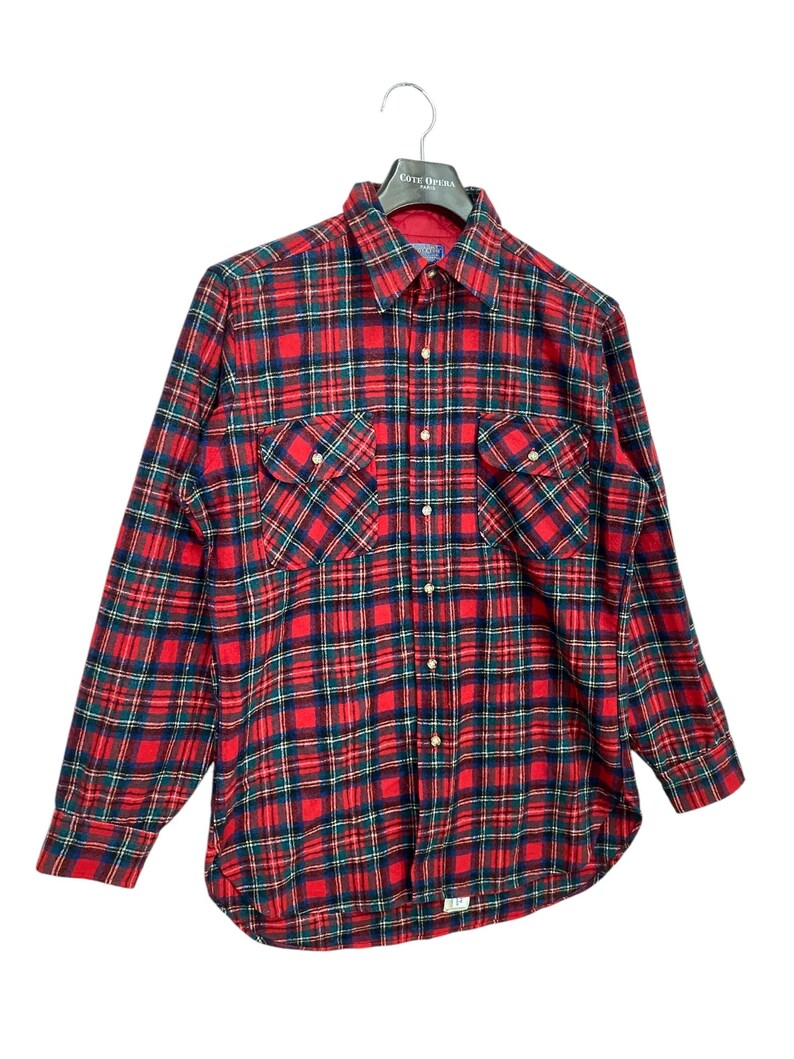 Puede incluir: Camisa de franela a cuadros rojos y verdes con mangas largas y cierre de botones. La camisa tiene dos bolsillos de solapa en el pecho.
