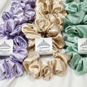 May include: Three satin scrunchies in lavender, beige, and mint green with a crown and the text "Alannah's Sweet 16 04.18.2023" printed on a white tag.