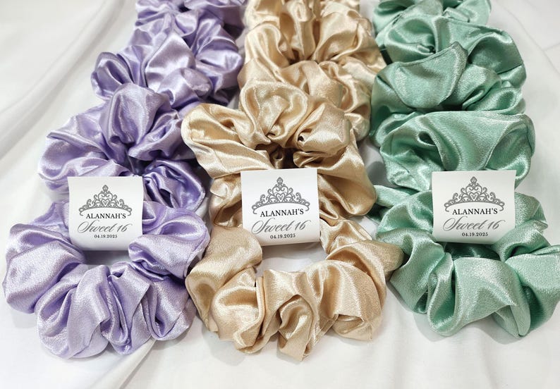 May include: Three satin scrunchies in lavender, beige, and mint green with a crown and the text "Alannah's Sweet 16 04.18.2023" printed on a white tag.