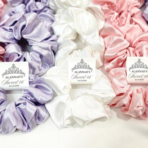 May include: Three satin scrunchies in lavender, white, and pink with personalized tags that say "Alannah's Sweet 16" with a date.