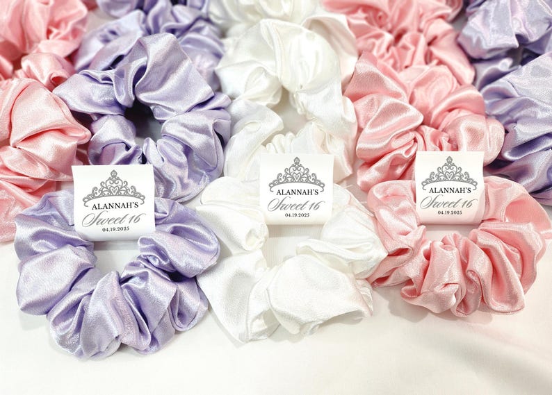 May include: Three satin scrunchies in lavender, white, and pink with personalized tags that say "Alannah's Sweet 16" with a date.