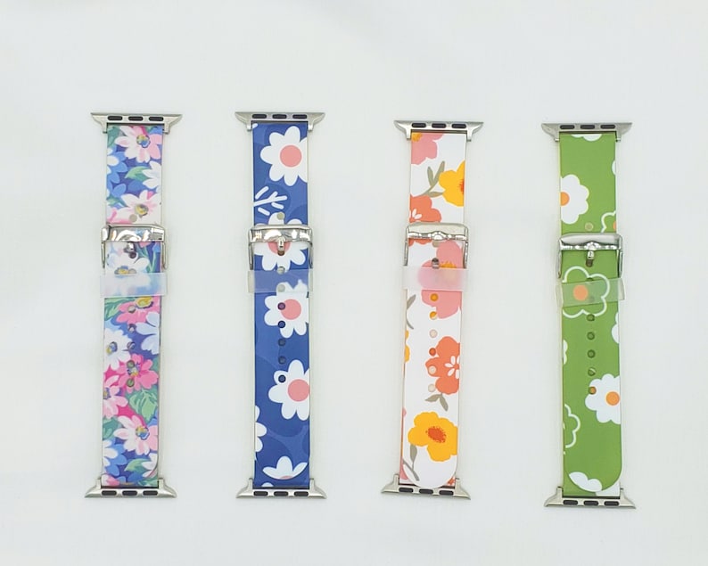 K&ouml;nnte beinhalten: Vier verschiedene Apple Watch Armb&auml;nder mit Blumenmustern. Die Armb&auml;nder sind in Blau, Gr&uuml;n, Wei&szlig; und Rosa mit wei&szlig;en Blumen.