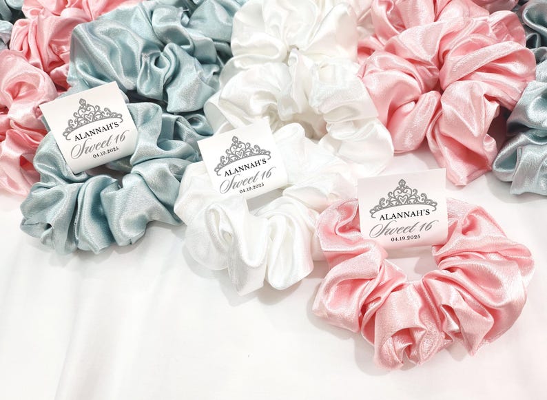 May include: Three satin scrunchies in light blue, white, and pink with a personalized tag that reads "Alannah's Sweet 16 04.19.2023".