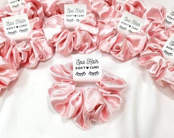 Peut inclure: Des chouchous en satin rose avec des étiquettes blanches qui disent "Spa Hair Don't Care!" avec un cœur et un graphique de cils.