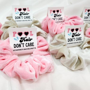 May include: Set of six pink and beige scrunchies with a white sticker attached to each one. The sticker says "POOL Hair Don't Care" with a heart-shaped sunglasses graphic. The text below the graphic says "[Name]'s Bachelorette".