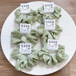 May include: Six sage green scrunchies with white square tags that say "NASH Bash" with a ring symbol.