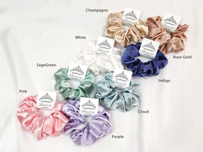 May include: Assortment of ten satin scrunchies in various colors, including pink, sage green, white, champagne, rose gold, indigo, cloud, and purple. Each scrunchie has a small tag attached with the text "Alannah's Sweet 16".