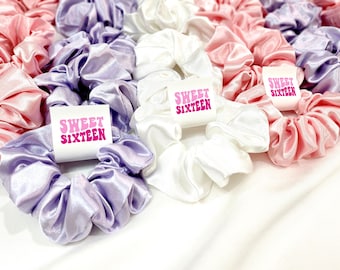 May include: A set of three satin scrunchies in lavender, white, and pink with "Sweet Sixteen" printed on each. The scrunchies are made of soft, silky fabric and are perfect for adding a touch of elegance to any hairstyle.
