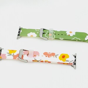 K&ouml;nnte beinhalten: Zwei Apple Watch Armb&auml;nder mit Blumenmustern. Das obere Armband ist gr&uuml;n mit wei&szlig;en Blumen. Das untere Armband ist wei&szlig; mit rosa und gelben Blumen.