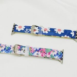 K&ouml;nnte beinhalten: Zwei Apple Watch Armb&auml;nder mit Blumenmustern. Das obere Armband hat ein wei&szlig;es und pinkfarbenes Blumenmuster auf blauem Hintergrund. Das untere Armband hat ein wei&szlig;es und blaues Blumenmuster auf blauem Hintergrund.
