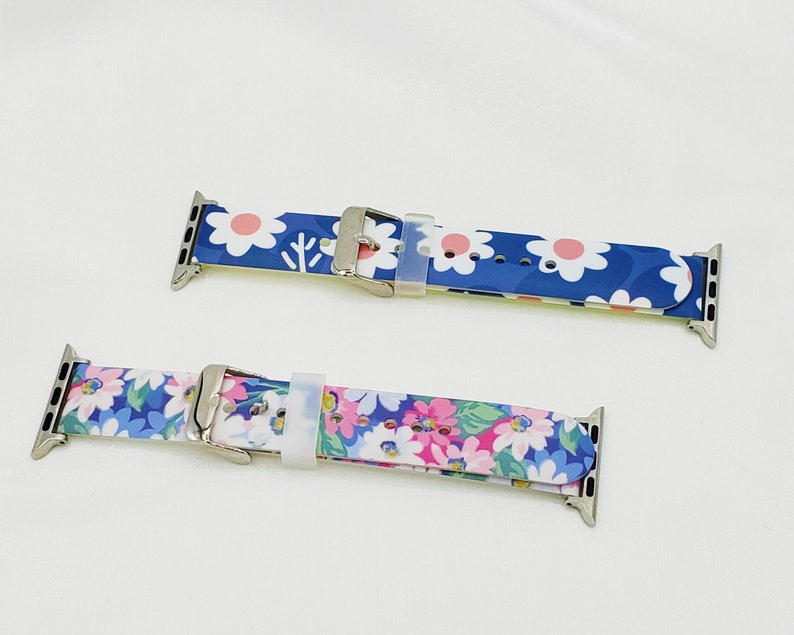 K&ouml;nnte beinhalten: Zwei Apple Watch Armb&auml;nder mit Blumenmustern. Das obere Armband hat ein wei&szlig;es und pinkfarbenes Blumenmuster auf blauem Hintergrund. Das untere Armband hat ein wei&szlig;es und blaues Blumenmuster auf blauem Hintergrund.