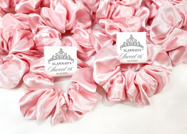 May include: Pink satin scrunchies with white tags that say "Alannah's Sweet 16" with a crown graphic and the date "04.19.2025".