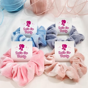 K&ouml;nnte beinhalten: Vier Samt-Haargummis mit wei&szlig;en Etiketten, auf denen "Let's Go Party" mit einer rosa Silhouette eines Frauenkopfes steht. Die Haargummis sind in Blau, Rosa und Hellrosa.