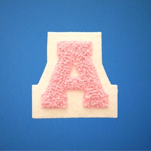 May include: A pink felt letter A on a white background. The letter is surrounded by a white border.