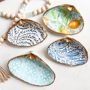 May include: Four decorative seashell-shaped dishes with gold trim. Each dish features a different blue and white patterned design.