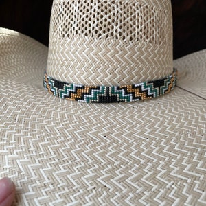 May include: A straw cowboy hat with a black, white, gold, and green beaded band.