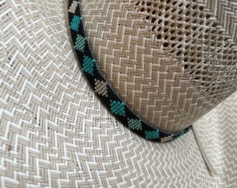 May include: A light beige woven straw hat featuring a decorative band made of small beads. The band is primarily black with a repeating geometric pattern of diamond shapes in alternating colors of turquoise blue and metallic silver.