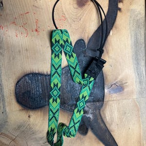 May include: A green and black beaded guitar strap with a black adjustable strap and a black buckle.