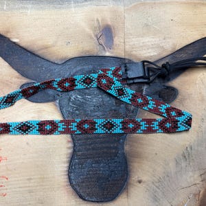 May include: A turquoise, brown, and black beaded guitar strap with a leather end and a tassel.