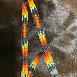 May include: A beaded camera strap with a geometric pattern in shades of orange, yellow, white, and green. The strap has a black leather end with a loop.