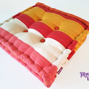 May include: A striped floor cushion with red, white, and yellow stripes. The cushion has a tufted design with buttons.