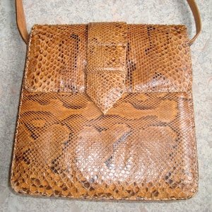 Peut inclure: Sac bandoulière rectangulaire en peau de serpent marron avec fermeture à rabat et bandoulière assortie. Le sac présente un motif texturé et un détail de boucle sur le devant.