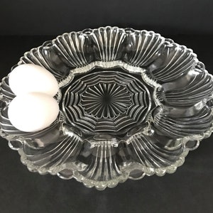 May include: A clear glass serving dish with scalloped edges and a central, starburst-patterned section. Two white eggs are placed in the dish.
